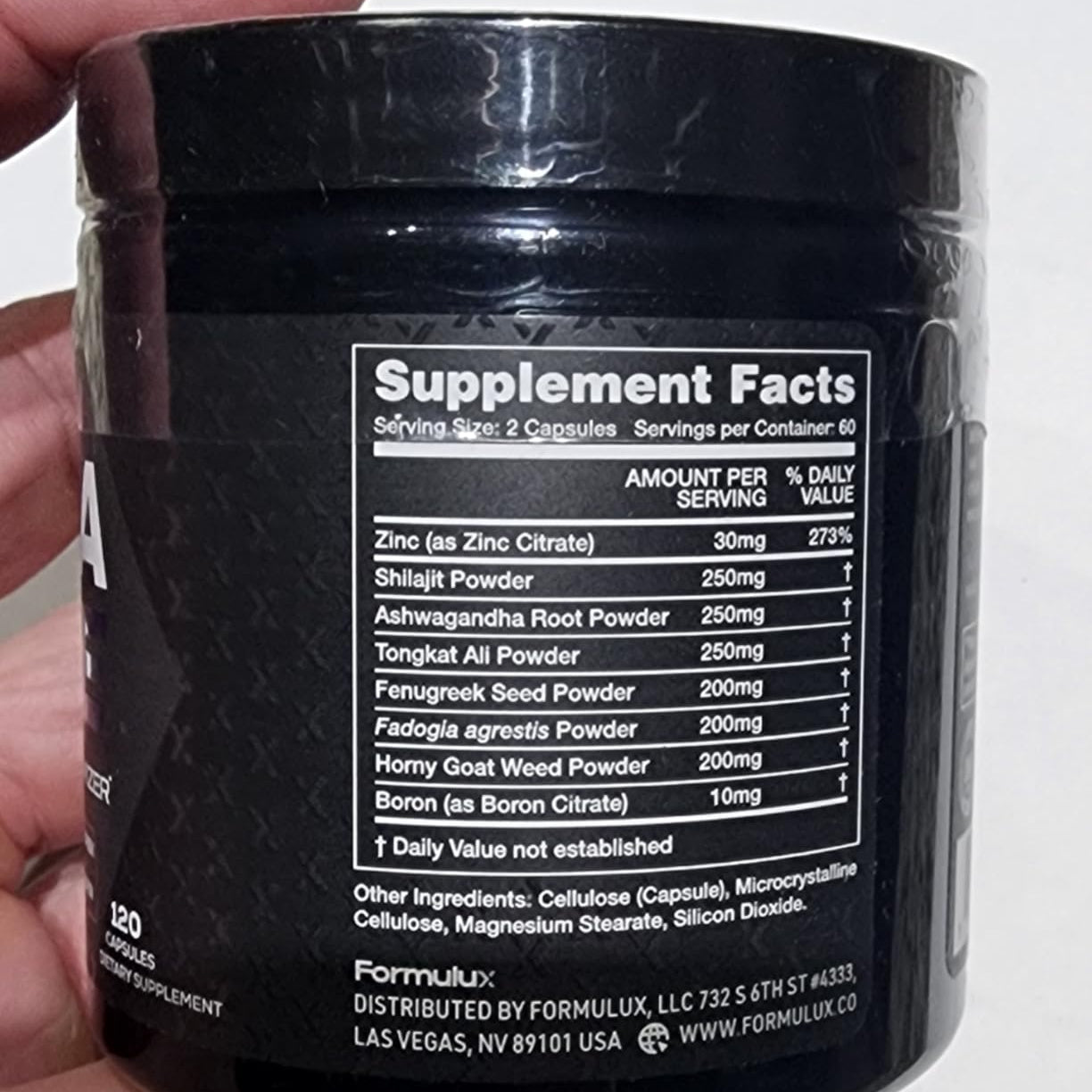 Black supplement container with ingredient list held by a hand on a white background